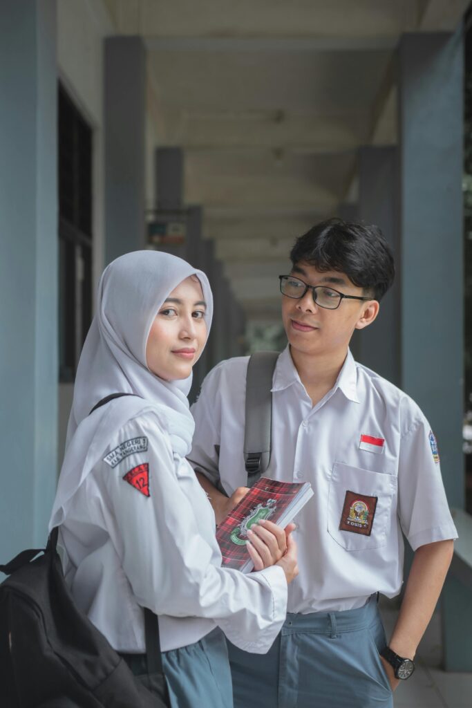 Two high school students in uniforms standing together, sharing a moment on campus.